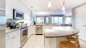 Een moderne keuken met witte kastjes, roestvrijstalen apparatuur, een granieten aanrechtblad en een centraal eiland met krukken.