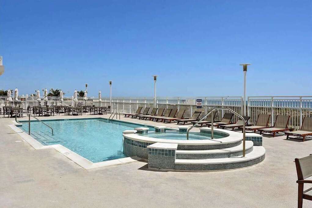 A pool area with a hot tub, lounge chairs, and a view of the ocean.
