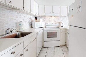 A compact kitchen with white cabinetry, a microwave, an oven, and a sink. - Fountainhead Towers 606 (Ocean City)