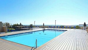 Un espace piscine doté d’une terrasse en bois, d’un plongeoir et offrant une vue dégagée sur la mer.