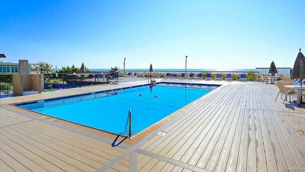 Area piscina con terrazza in legno, lettini e vista sul mare.