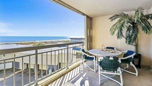 Un balcone con vista sull'oceano, un tavolo con sedie e una palma in vaso.
