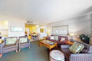 A living room with striped sofas, a coffee table, and a dining area in the background. - Fountainhead Towers 405 (Ocean City)