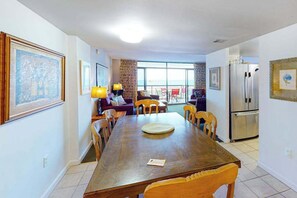 A dining area with a wooden table, chairs, a refrigerator, and a view of the sea. - Fountainhead Towers 405 (Ocean City)