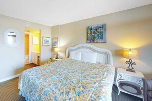 A hotel room with a bed, bedside tables, a mirror, a painting, and a door leading to a bathroom. - Fountainhead Towers 405 (Ocean City)
