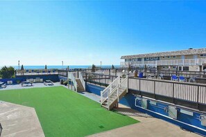 A beachfront hotel with a pool, a grassy area, and a staircase leading to the upper level. - Steps to the beach - condo with 2 balconies, central AC & pool (Ocean City)