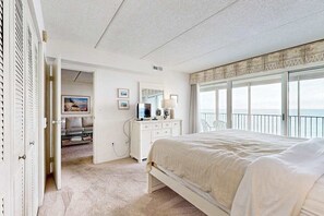 A bedroom with a large bed, a dresser, a television, and a view of the ocean. - Beachfront condo with indoor pool, new fitness center, ocean & beach views (Ocean City)