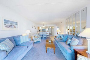 Ein Wohnzimmer mit einer Sofagarnitur, einem Couchtisch und einem Essbereich im Hintergrund.