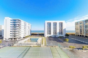 Ein modernes Gebäude mit mehreren Balkonen, einem Tennisplatz und Blick aufs Meer.