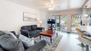 A living room with a sofa, a coffee table, a TV, and a view through a glass door. - Drawbridge Rd 38 (Ocean Pines)