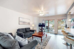 Ein Wohnzimmer mit einer Couch, einem Couchtisch, einem Fernseher und Blick durch eine Glastür.