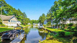 A canal with boats docked on a wooden pier, surrounded by lush greenery and residential buildings. - Drawbridge Rd 38 (Ocean Pines)