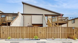 A two-story building with a wooden deck, a ramp, and a gated entrance. - Club Ocean Villa II 144 (Ocean City)