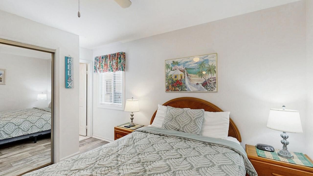 A bedroom with a bed, nightstands, a mirror, a window with blinds, and a painting on the wall.