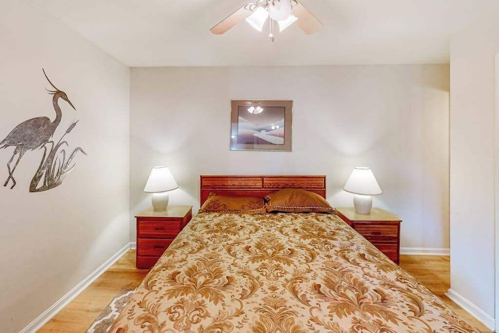 Een slaapkamer met een bed, twee nachtkastjes met lampen, een plafondventilator, een ingelijst kunstwerk aan de muur en een muurstickers van een vogel.