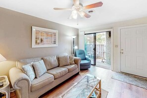 A living room with a sofa, a chair, a ceiling fan, a framed picture, and a sliding glass door leading to an outdoor area. - Club Ocean Villa II 74 (Ocean City)