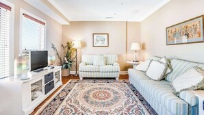 Una sala de estar con televisor, sofá, sillón y un tapete estampado.