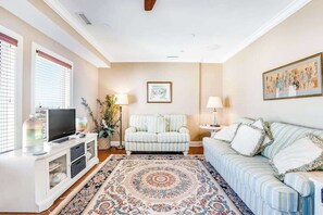 Ein Wohnzimmer mit Fernseher, Sofa, Sessel und einem gemusterten Teppich.