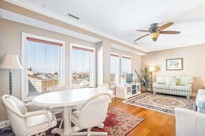 Ein geräumiges Wohnzimmer mit Essbereich, großen Fenstern, einem Deckenventilator und Blick auf die Stadt.