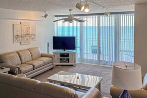 Ein Wohnzimmer mit einer Couch, einem Couchtisch, einem Fernseher und einem Balkon mit Blick.