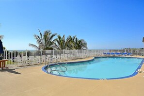 Ein Pool mit weißem Zaun, blauen Stühlen und Palmen.