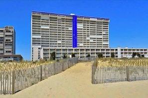 Ein großes Hotel mit mehreren Etagen, einem sandigen Weg, der zum Eingang führt, und einem strahlend blauen Himmel.