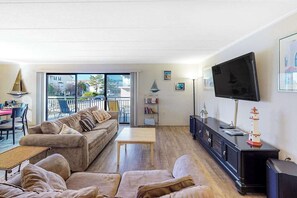 A living room with a sofa, a TV, a small table, and a balcony with outdoor furniture. - Diamond Beach 117 (Ocean City)