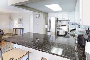 A modern kitchen with a granite countertop, stainless steel appliances, and white cabinetry. - Diamond Beach 117 (Ocean City)