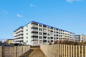 A multi-story hotel with balconies, a sandy path leading to the entrance, and a wooden fence. - Diamond Beach 117 (Ocean City)