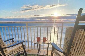 Ein Balkon mit Blick auf das Meer, zwei Stühle, ein kleiner Tisch mit zwei roten Tassen und ein stuhl mit Muster.