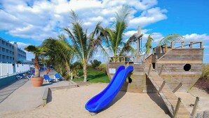 Ein Strand mit einer blauen Rutsche, Palmen und einer Holzkonstruktion.