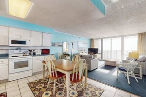 A modern kitchen with white cabinets, a dining table with chairs, a sofa, and a TV. - Convenient beachfront condo with fast WiFi, pools, sauna, gym, & central A/C (Ocean City)