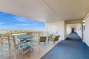 Een balkon met een tafel en stoelen, een gang met deuren en uitzicht op de stad.