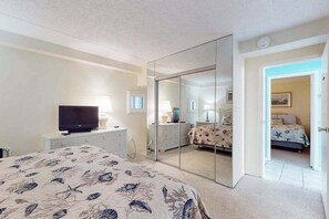 Een slaapkamer met een bed, een televisie, een dressoir, een spiegel en een deur naar een andere kamer.