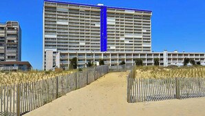 Ett stort hotell med flera våningar, en sandstig som leder till entrén och ett trästaket på vardera sidan.