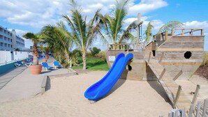 A beach with a blue slide, palm trees, and a wooden structure. - Carousel 807 (Ocean City)