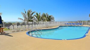 A swimming pool with a white fence, blue lounge chairs, and palm trees. - Carousel 807 (Ocean City)