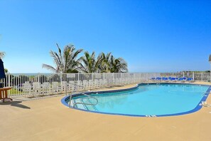 A swimming pool with a white fence, blue lounge chairs, and palm trees. - Carousel 807 (Ocean City)
