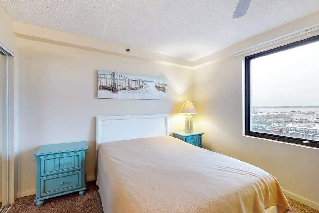 Une chambre d’hôtel avec un lit, une table de chevet, une lampe, une fenêtre donnant sur la ville et un tableau au mur.