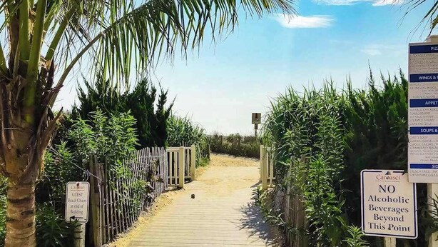 Een houten pad dat leidt naar strandstoelen, met een bord waarop staat dat alcoholische dranken verboden zijn vanaf een bepaald punt.