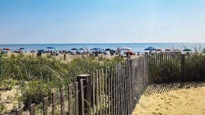 Een strand met een houten omheining, strandparasols en mensen in de verte.