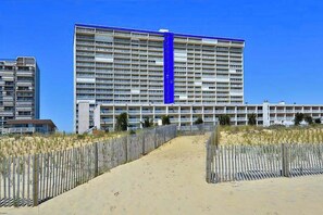 Ein großes Hotel mit mehreren Etagen, einem auffälligen, blauen vertikalen Streifen und einem Sandweg, der zum Eingang führt.