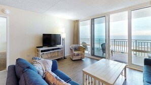 Een balkon met uitzicht op zee, een televisie op een standaard, een bank en een tafel.