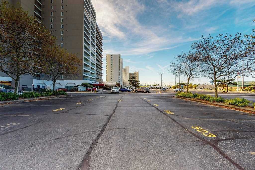 A parking lot with marked spaces, a building with multiple floors, and a clear sky.