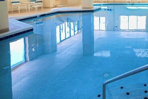 Une piscine à l’eau claire, avec un sol carrelé et des chaises blanches disposées tout autour.