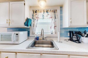 A kitchen with white cabinets, a stainless steel sink, a microwave, and a window with a curtain. - Top-floor, oceanfront condo w/ gorgeous view, balcony, beach access, & WiFi (Ocean City)