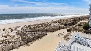 Vista sulla spiaggia con un sentiero sabbioso, una recinzione di legno e un edificio con un balcone.