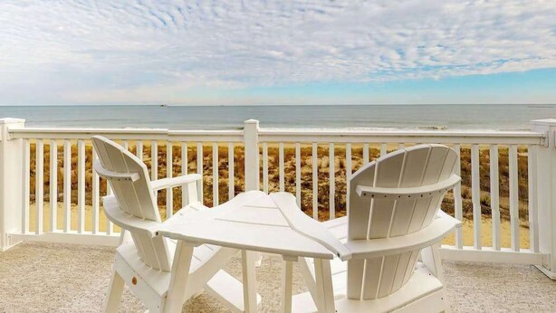 Una terrazza con sedie bianche e un tavolo con vista sulla spiaggia.