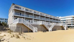 Un hotel a più piani con balconi, una spiaggia sabbiosa di fronte e un cielo azzurro limpido.