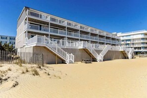 A multi-story hotel with balconies, a sandy beach in front, and a clear blue sky. - Caravelle 5 (Ocean City)